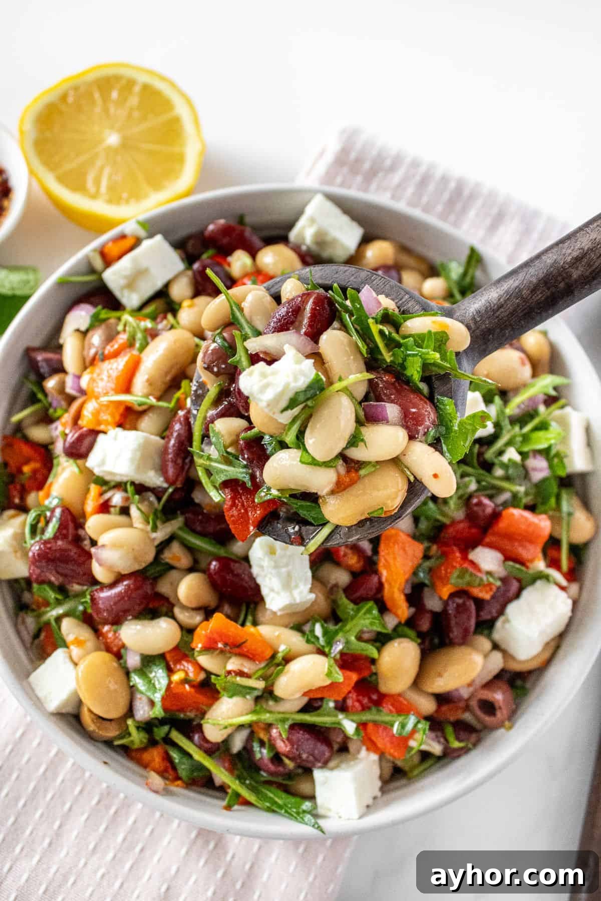 Spoon lifting up a serve of Mediterranean Bean Salad from a round white bowl.