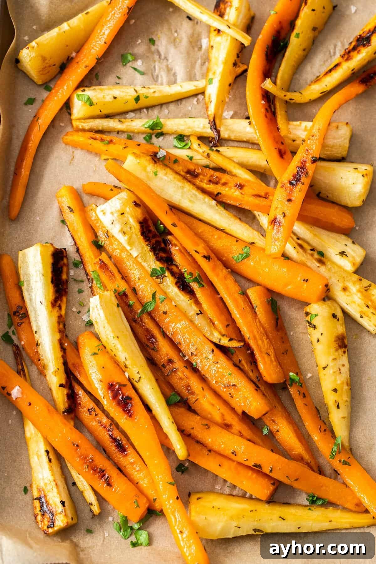 Baking tray with roasted carrots and parsnips, garnished with some fresh parsley.