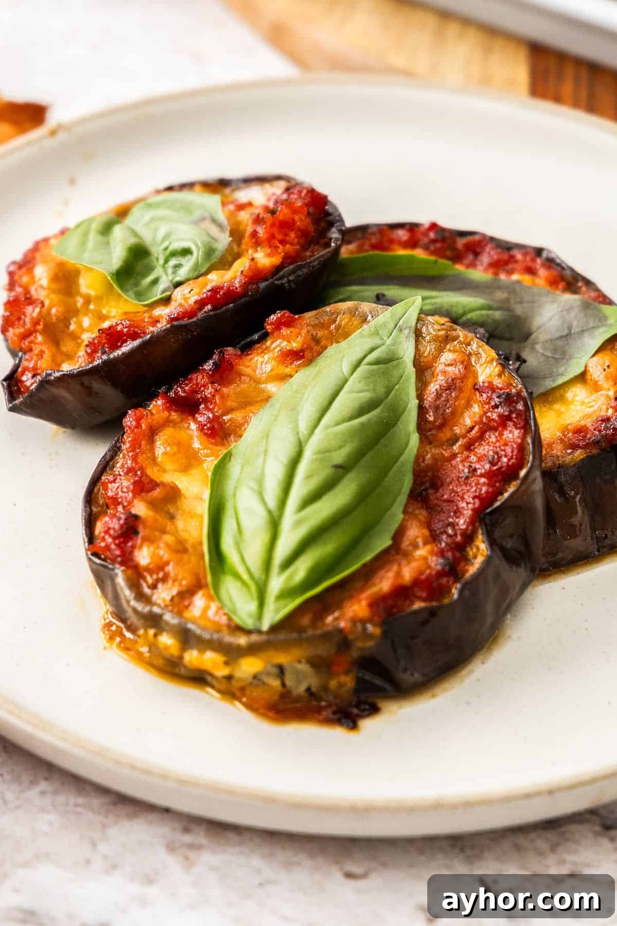Round white plate with three Baked Eggplant Slices, each topped with a fresh basil leaf.