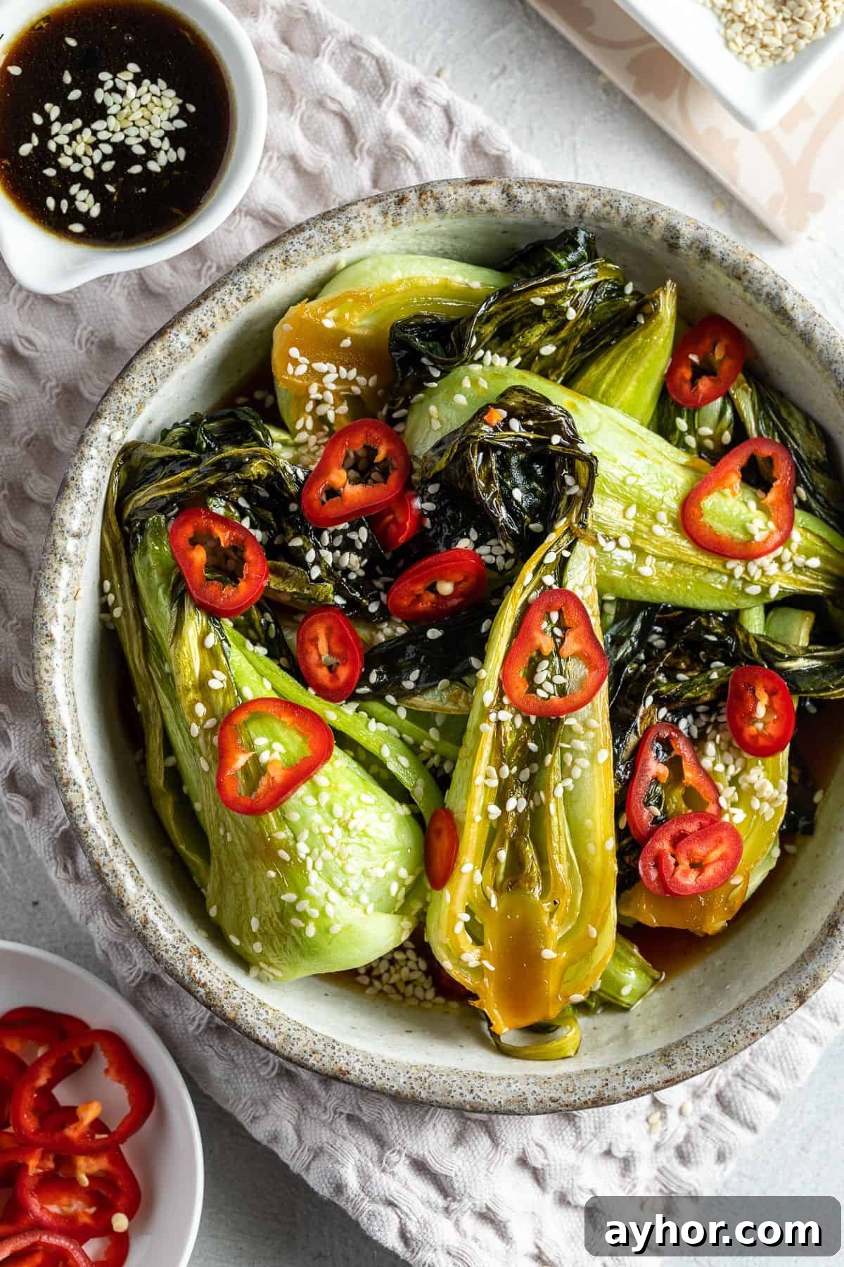 Round serving dish of bok choy, garnished with sesame seeds and fresh chilli.
