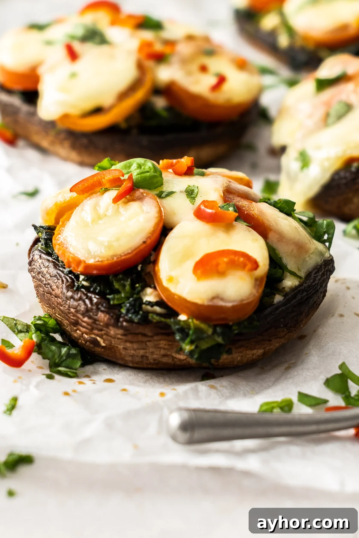Four Stuffed Portobello Mushrooms, garnished with chopped basil, sitting on some baking paper.