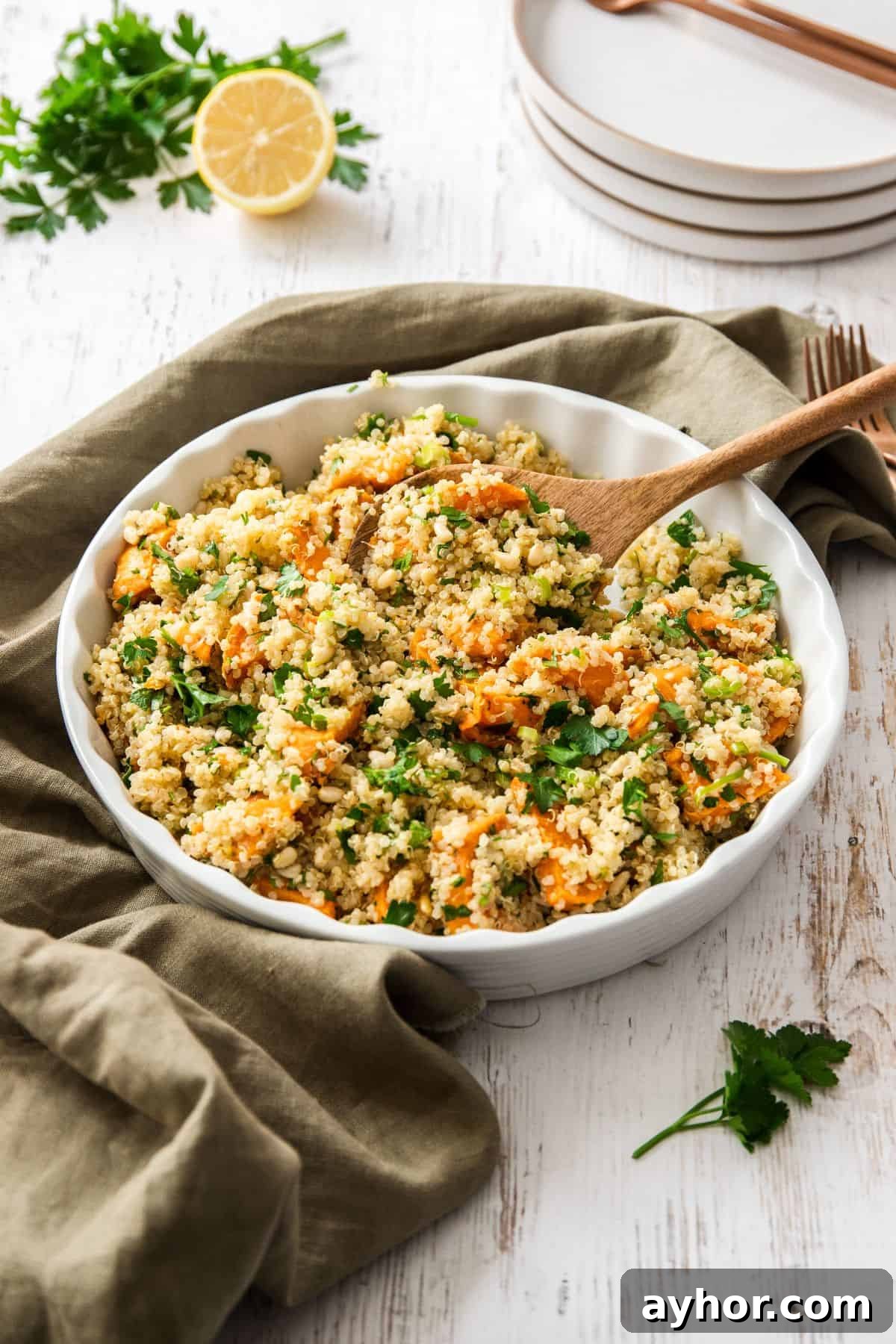 Round white dish of Sweet Potato and Quinoa Salad, with a wooden spoon resting in dish.