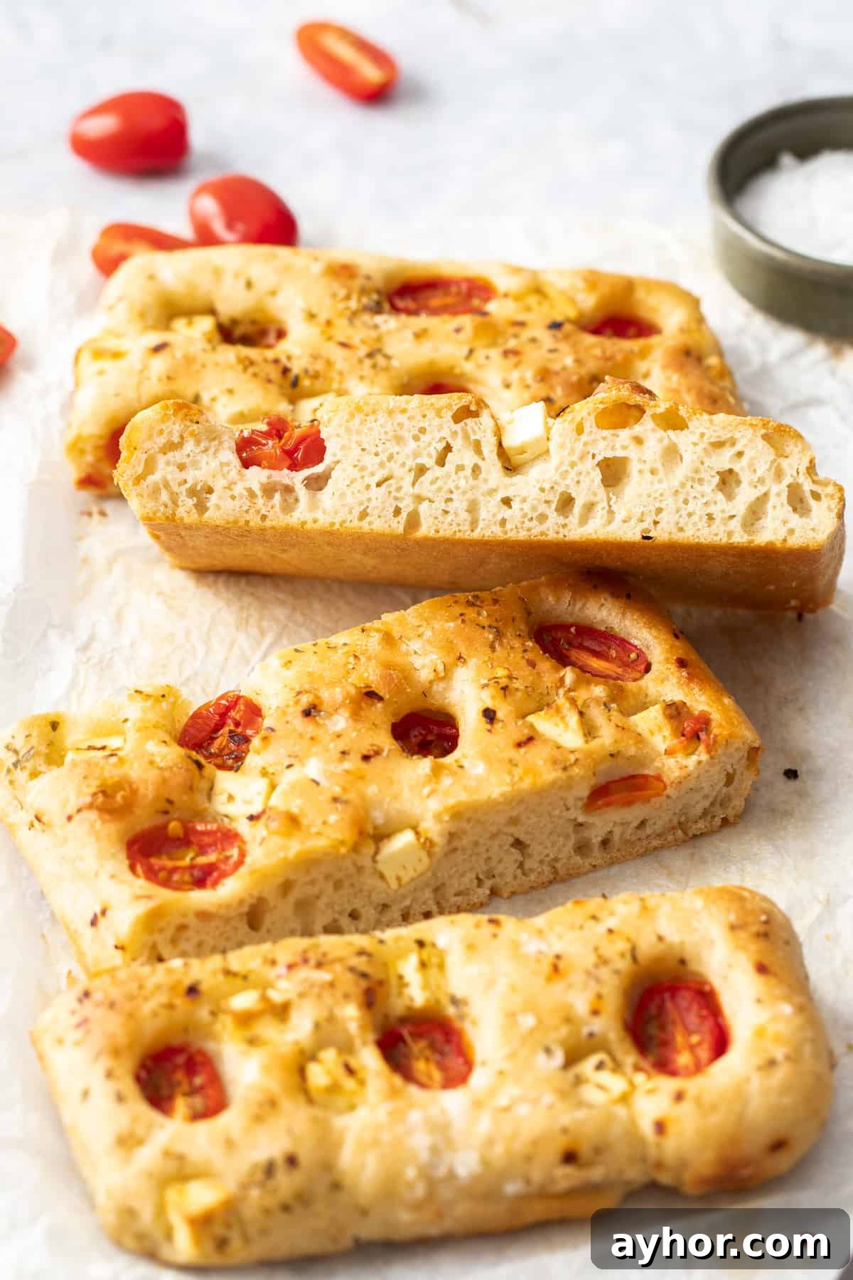 Four slices of focaccia, with one sitting on the edge to show the texture, sitting on some baking paper.