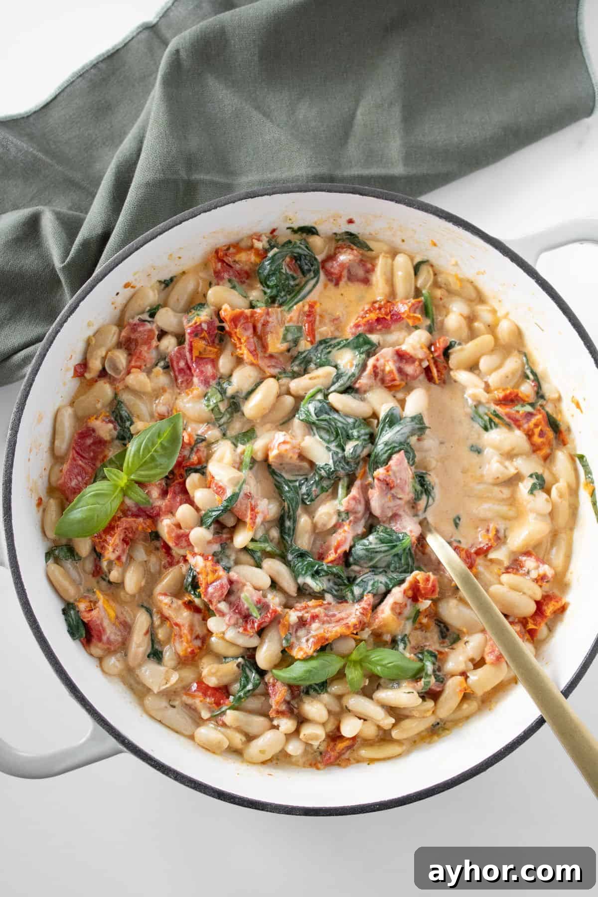 Round skillet with Creamy Sun-Dried Tomato Beans, with a spoon resting in the dish.