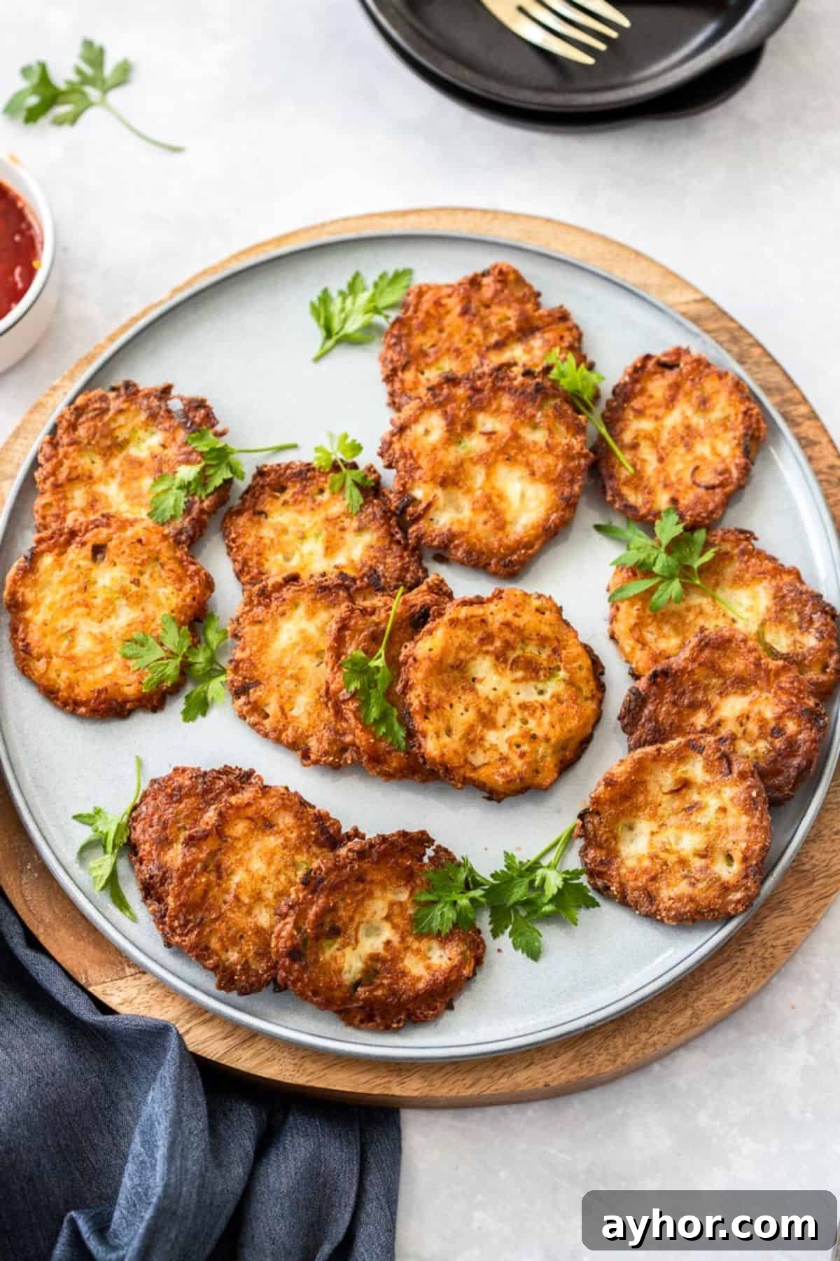 Round grey plate with cooked onion fritters, garnished with some parsley leaves, sitting on a round wooden board.