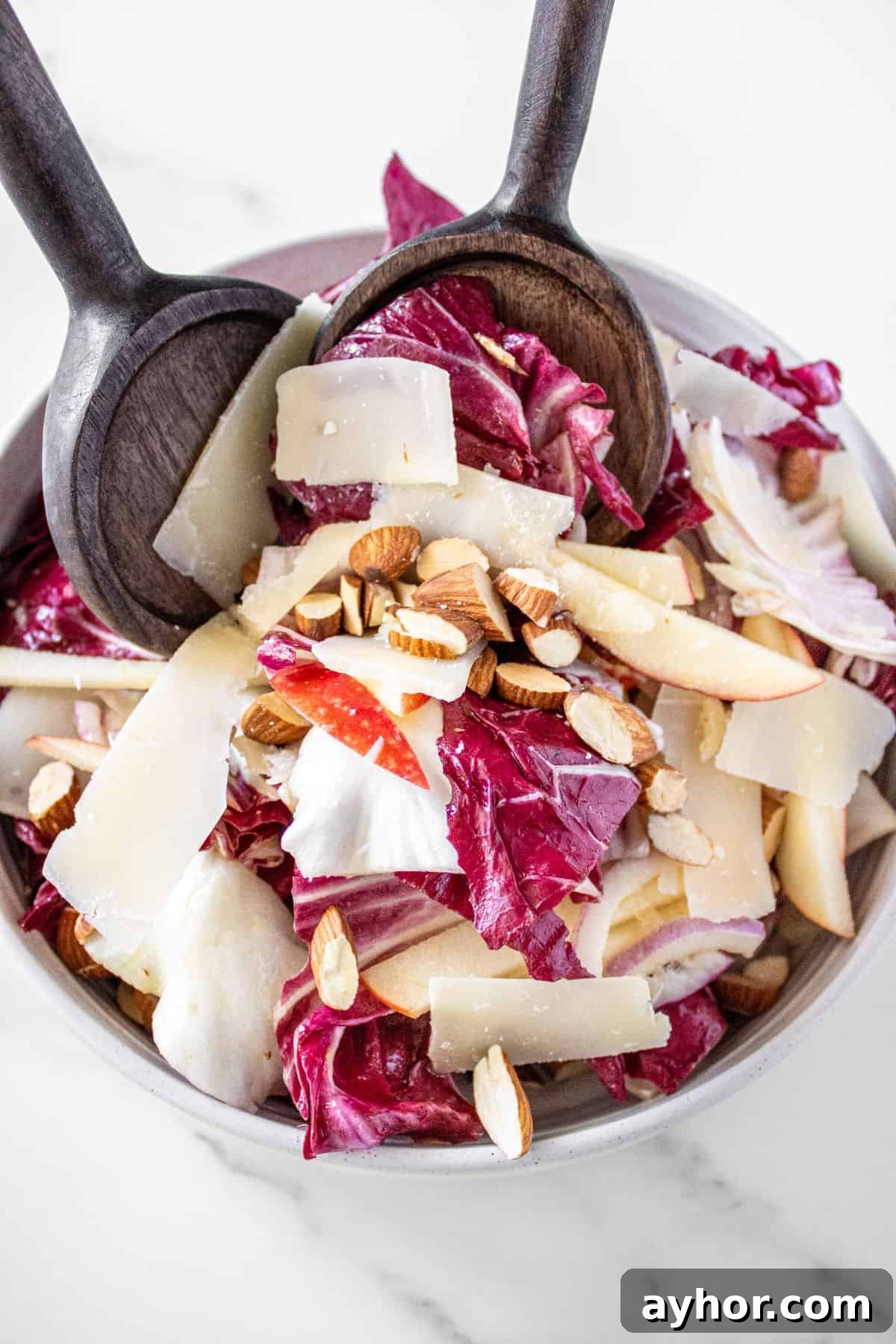 Round white bowl of Radicchio Salad with some wooden salad servers lifting some up.