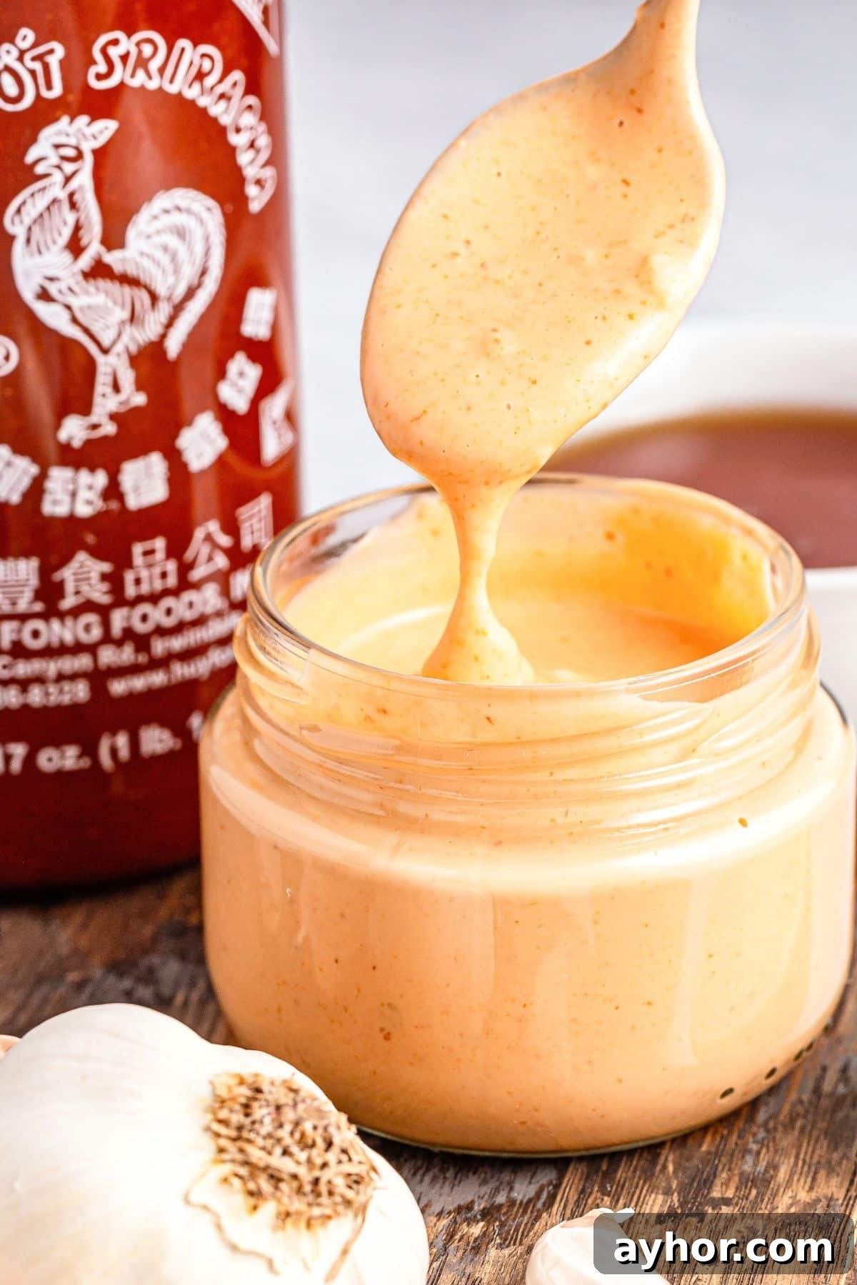 Sriracha Aioli Recipe (Gluten-Free, Dairy-Free) Holding up a spoonful of sriracha aioli from a jar.