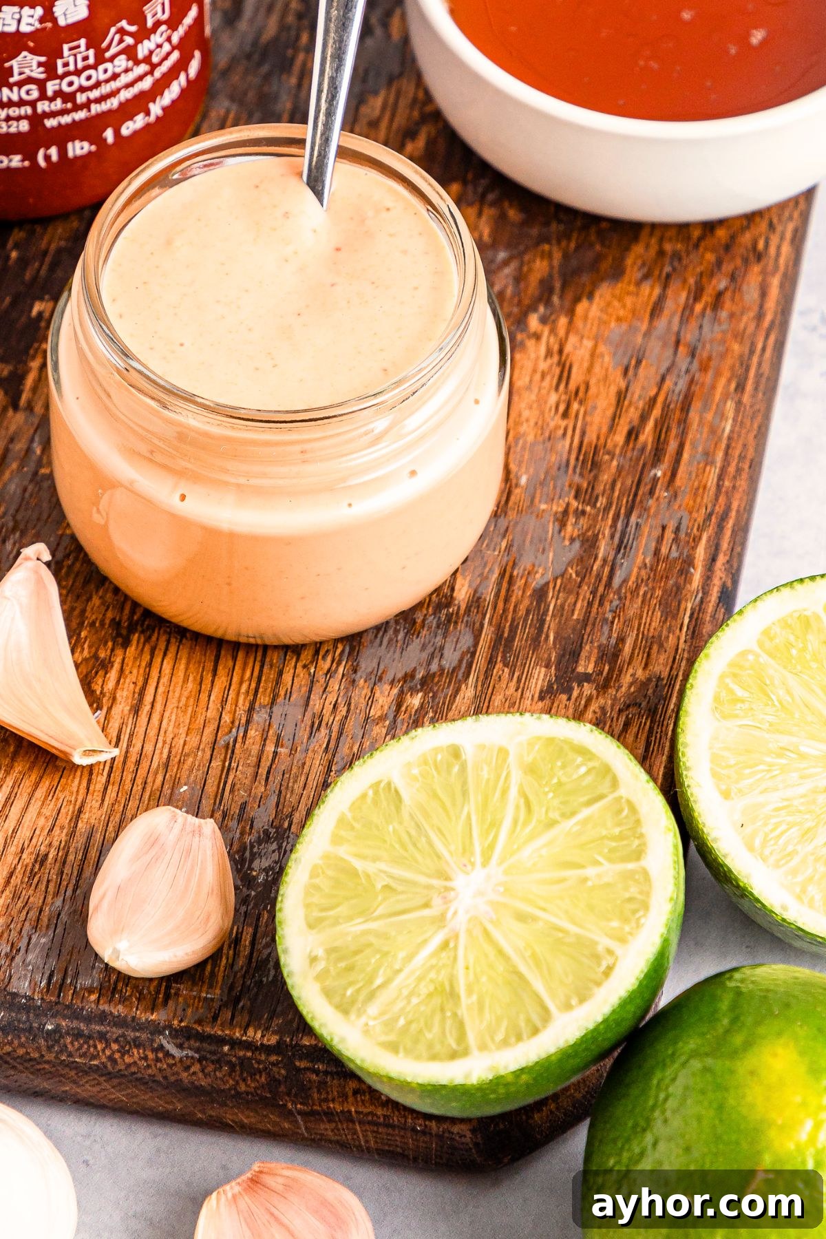 How to Make Sriracha Aioli A jar of homemade sriracha aioli on wooden board.