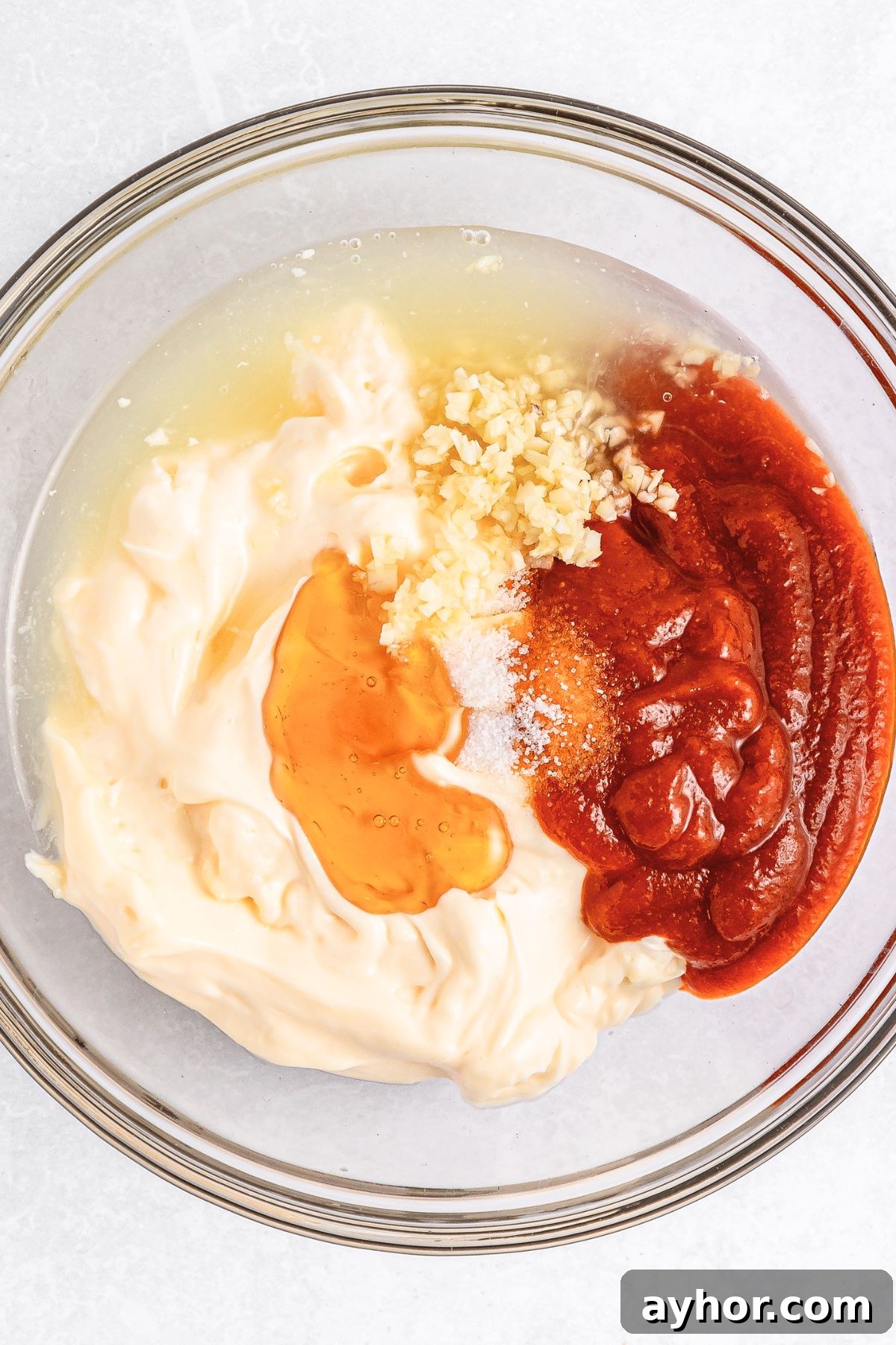 How to Make Sriracha Aioli (Gluten-Free, Dairy-Free) Sriracha sauce, mayonnaise, honey, minced garlic and lime juice in a glass bowl.