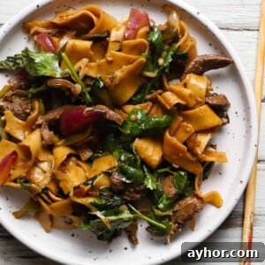 A plate of spicy Sichuan lamb noodles with vegetables and herbs.