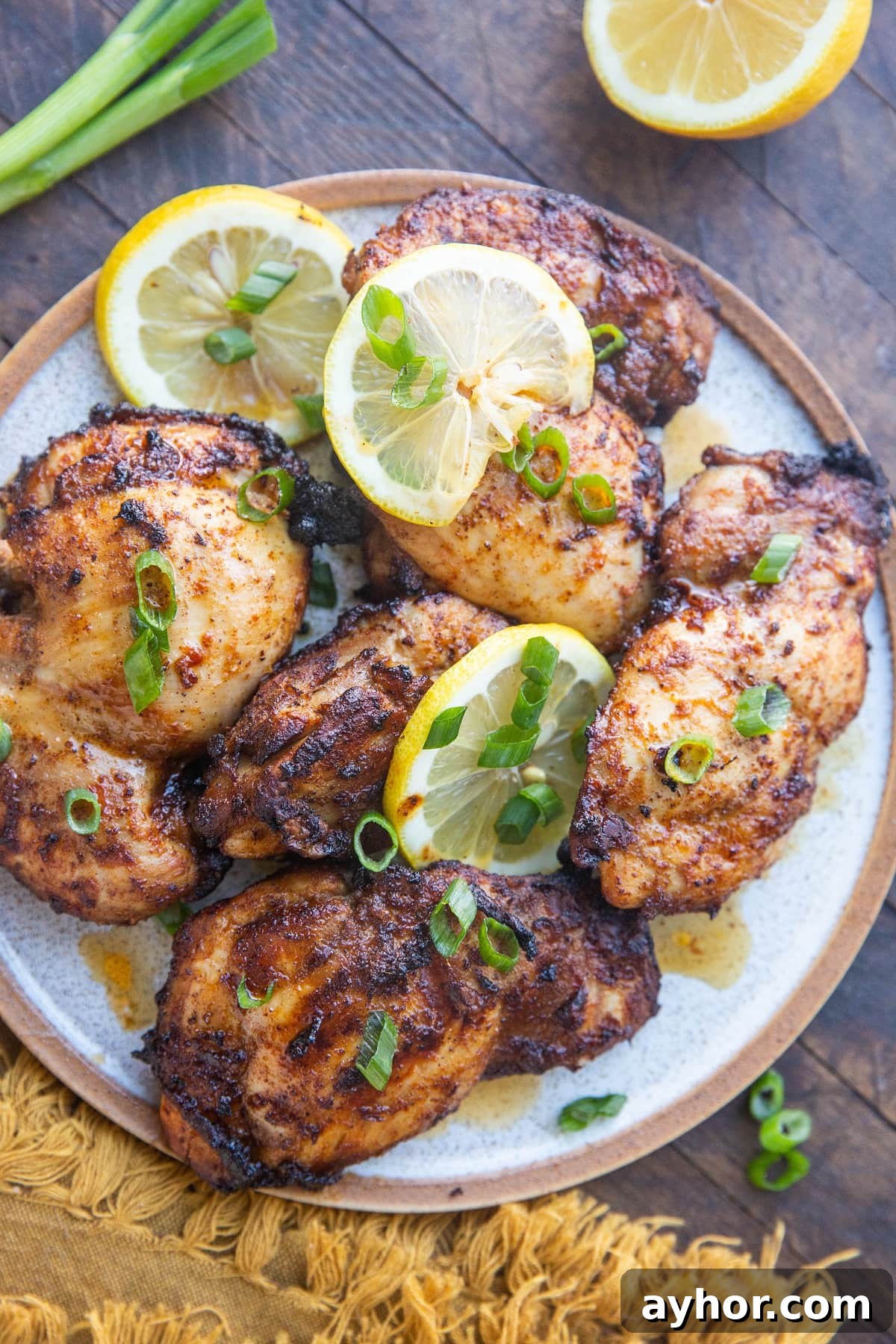 Crispy Mediterranean Chicken Thighs in the Air Fryer 2 Top down plate of Mediterranean chicken sprinkled with green onions and slices of lemon on a rustic wooden background.