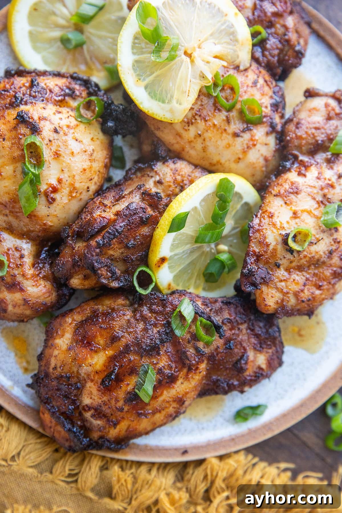 Crispy Mediterranean Chicken Thighs in the Air Fryer 11 Close up plate of chicken thighs on a plate with green onions and lemon slices.