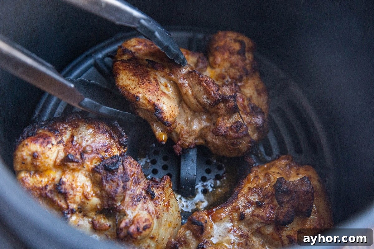 Crispy Mediterranean Chicken Thighs in the Air Fryer 8 Tongs flipping chicken thighs in an air fryer.
