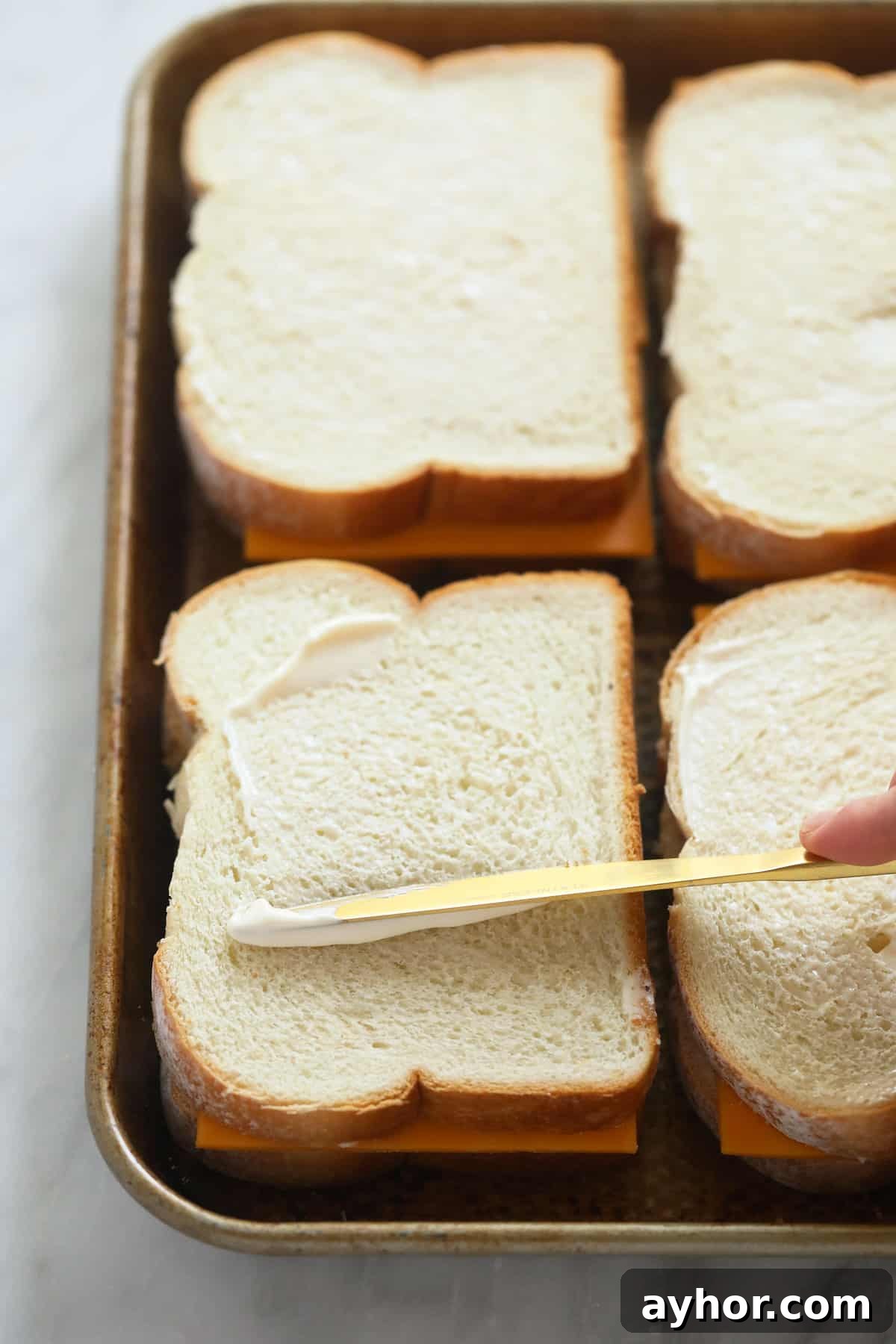 Buttering the bread sheet pan grilled cheese sandwiches being spread with butter on the outside of the bread
