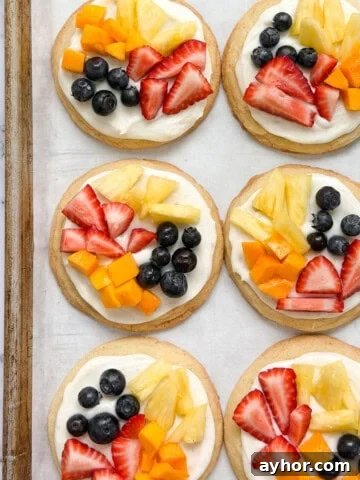 a few of the sugar cookie fruit pizzas on a cookie sheet.