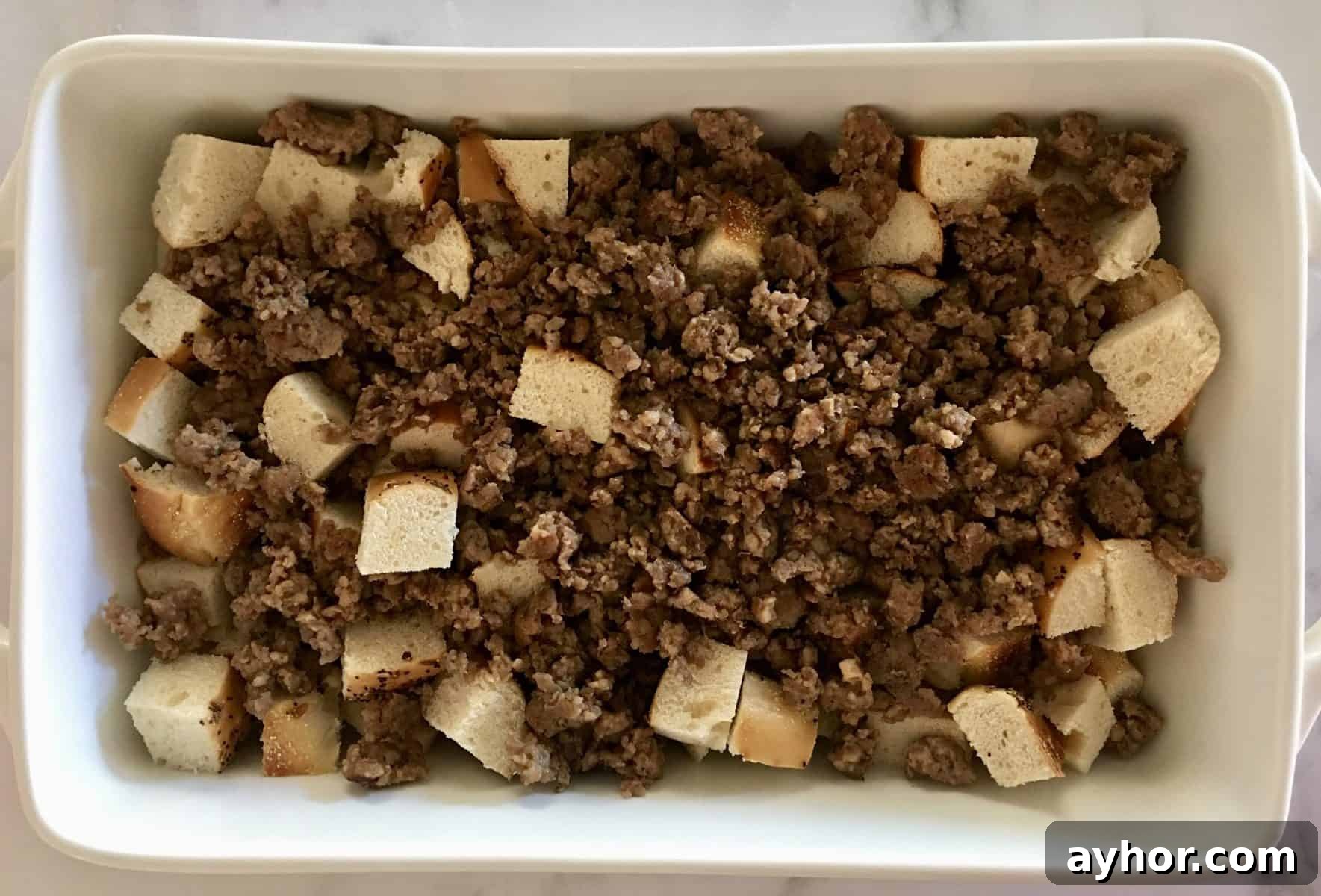 Everything Bagel Sausage Breakfast Bake 4 Cut up bread and cooked meat in a white casserole dish.